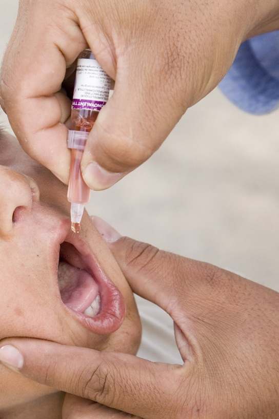Photo shows a child receiving an oral vaccination from a dropper.