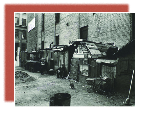 A photograph shows a row of urban shanties, with several of their inhabitants sitting outside.