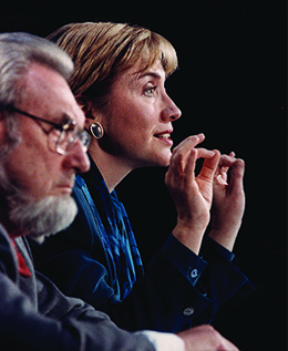 A photograph shows C. Everett Koop and Hillary Clinton in profile. They sit beside one another; Clinton speaks and gestures with her hands.